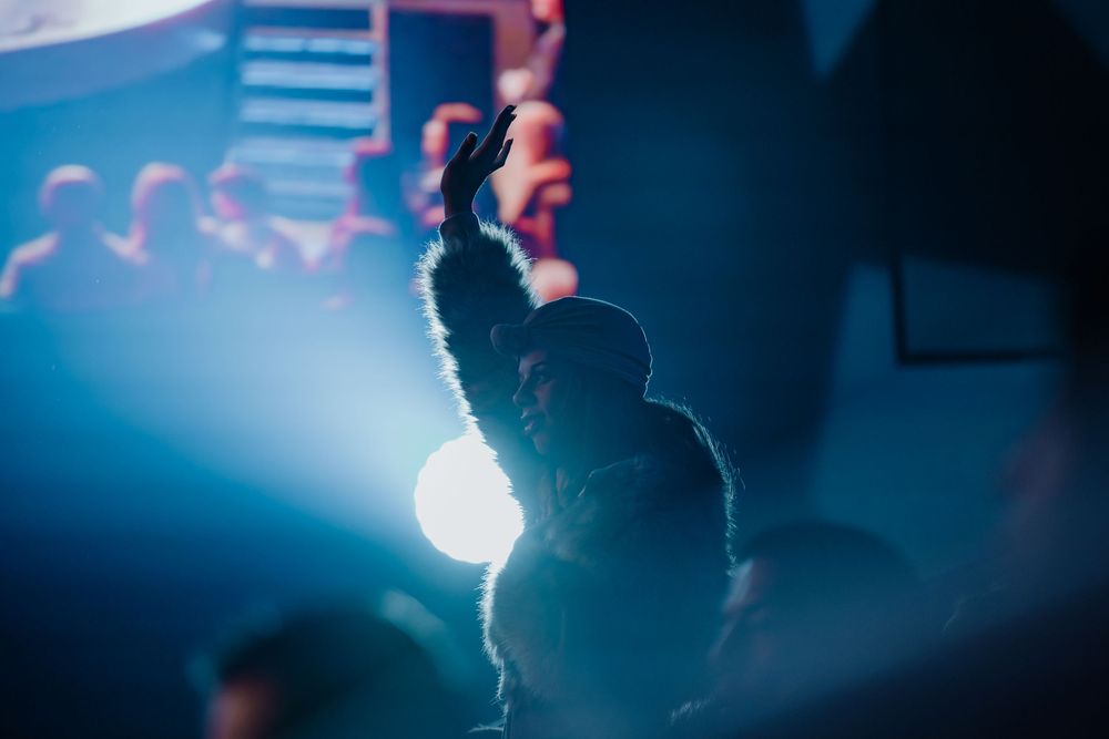 Concert attendee raises hand in the air amid bright blue stage lighting at a live music event.