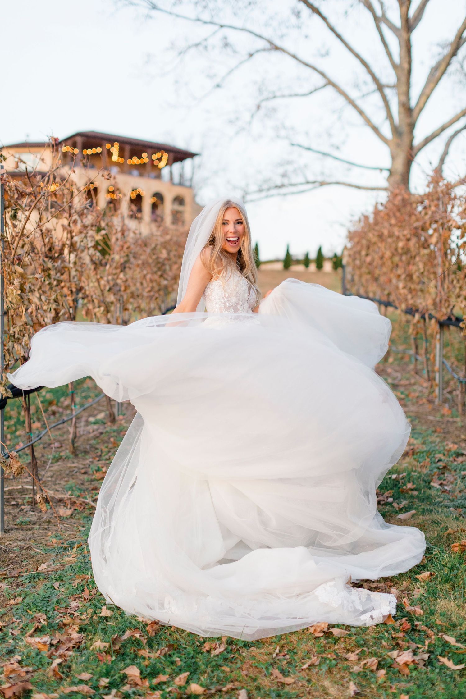 Joyful bride in flowing white tulle gown twirling outdoors at Montaluce Winery vineyard wedding venue during golden hour.