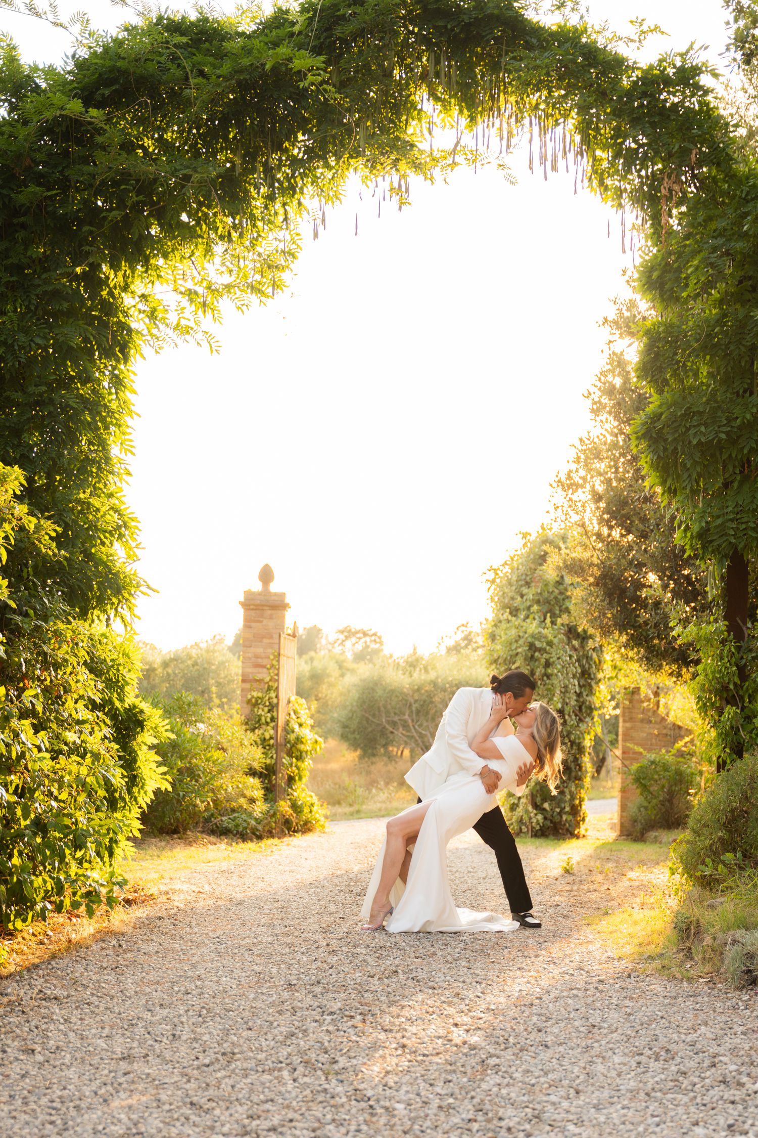 Black and white candid of a bride and groom kissing in an outdoor, tree-lined setting; authentic destination wedding and couple portraiture.
