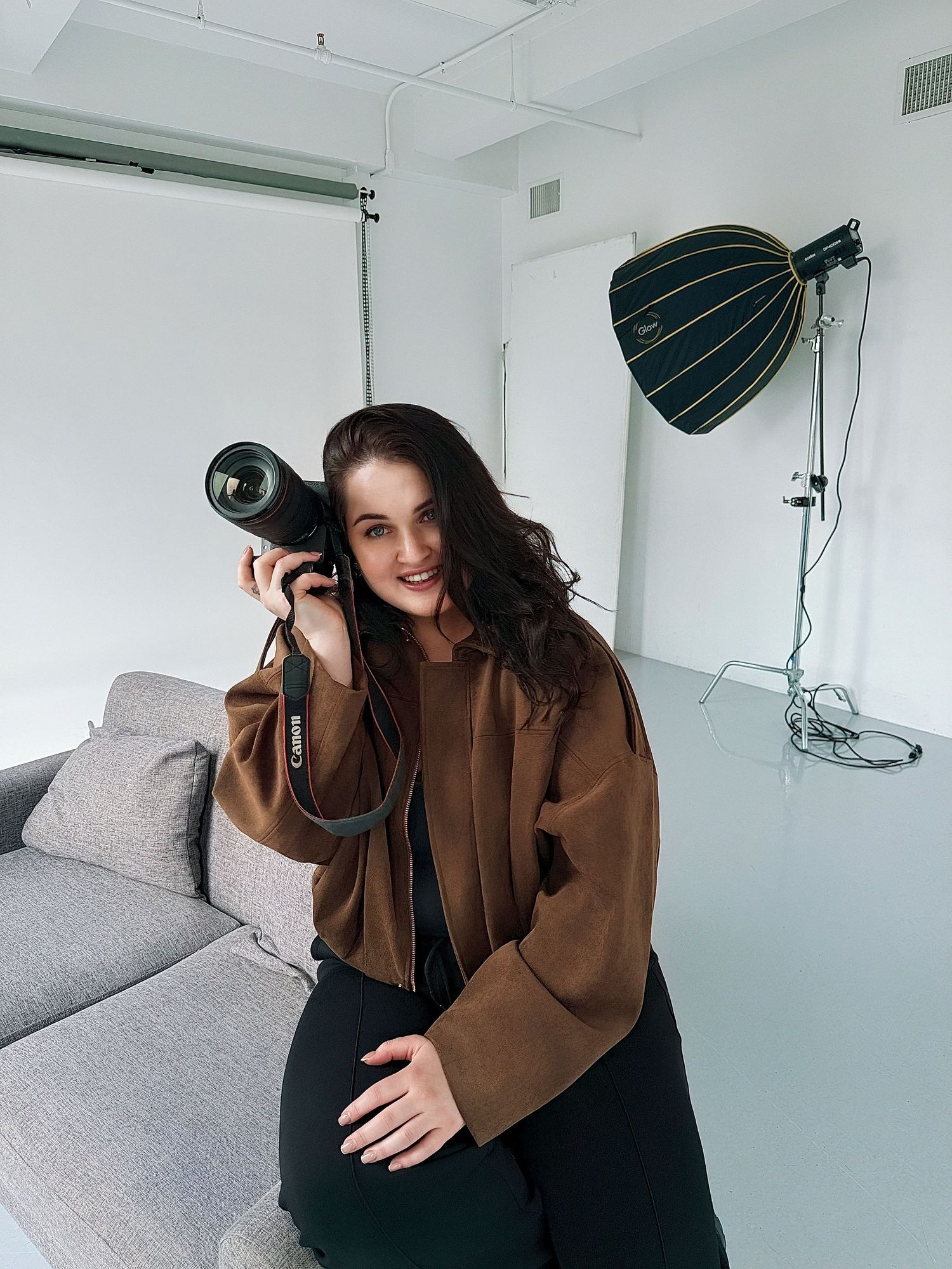 Photographer sitting in modern gold chair with studio lights and camera equipment.