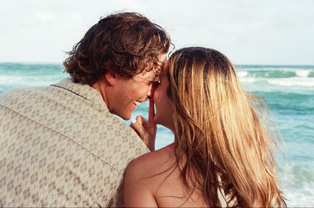 Kauai proposal photos with romantic couple sharing a sweet moment on the beach with turquoise ocean waves of Kauai in the background.