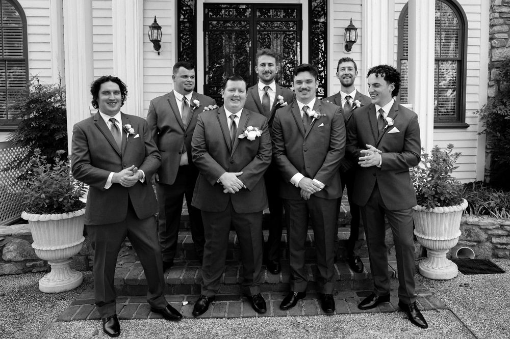 Groomsmen in formal suits pose together on front steps of white building in Nashville, TN.