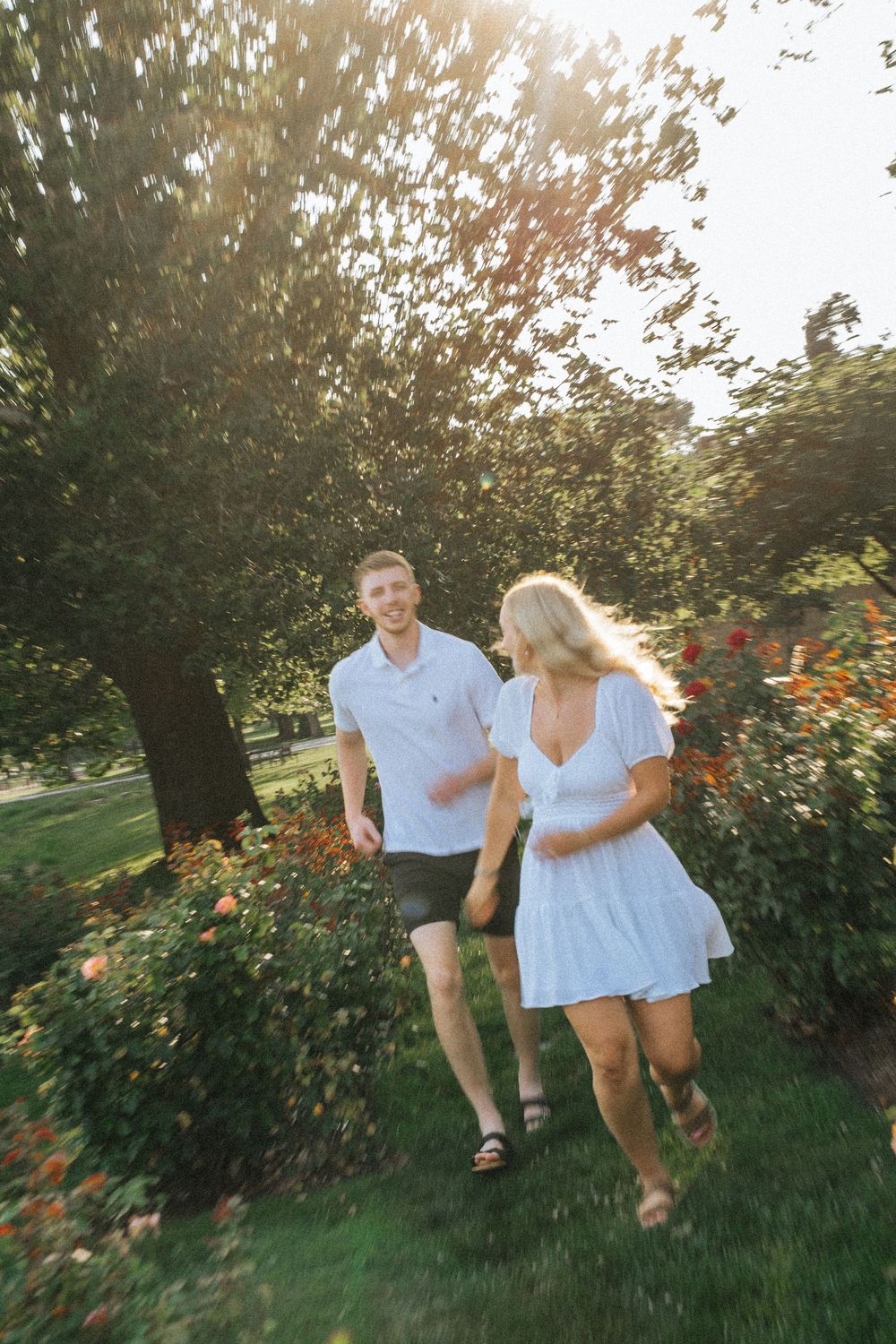 Playful couple runs through a garden with roses and greenery during sunset.