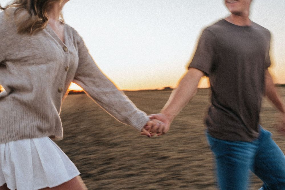 A couple holding hands while walking on a beach during sunset with warm lighting.