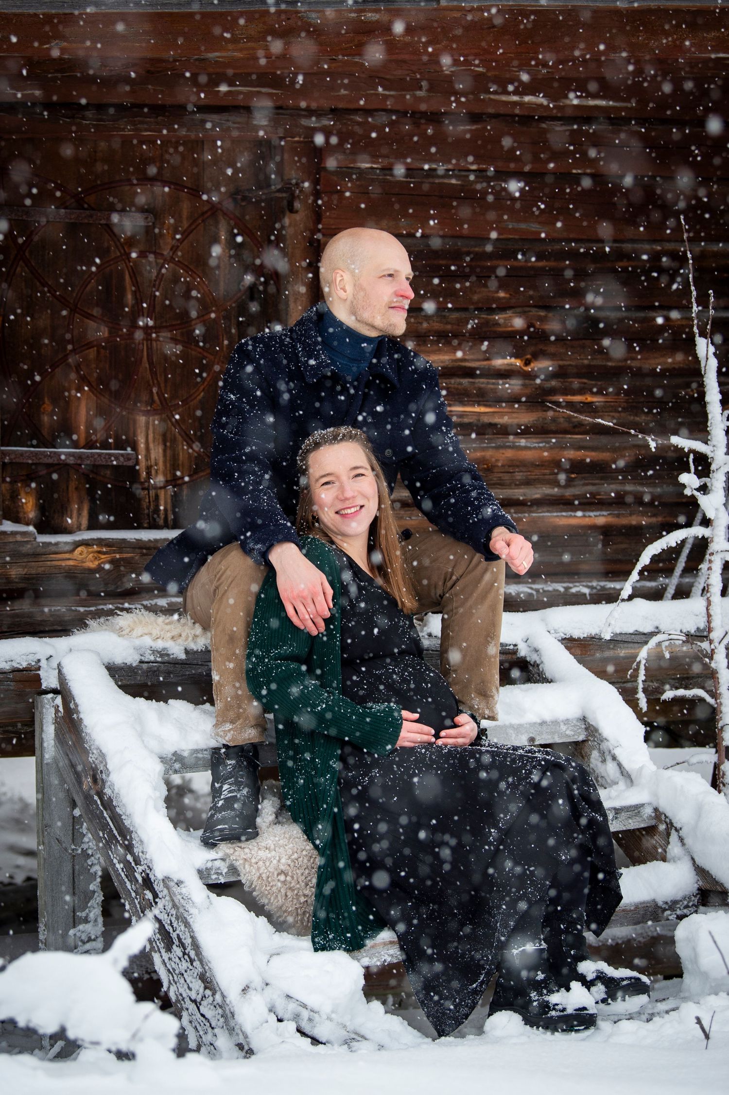Gravidfotografering i snöfall framför ett härbre