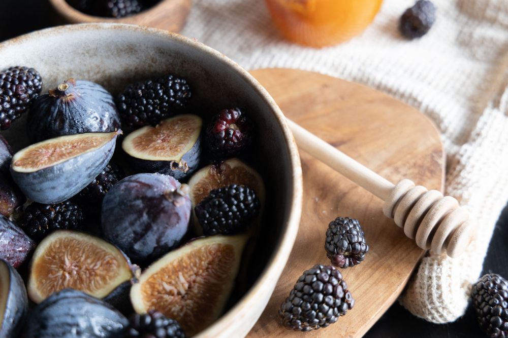 closeup of blackberries and figs in a bowl next to honey