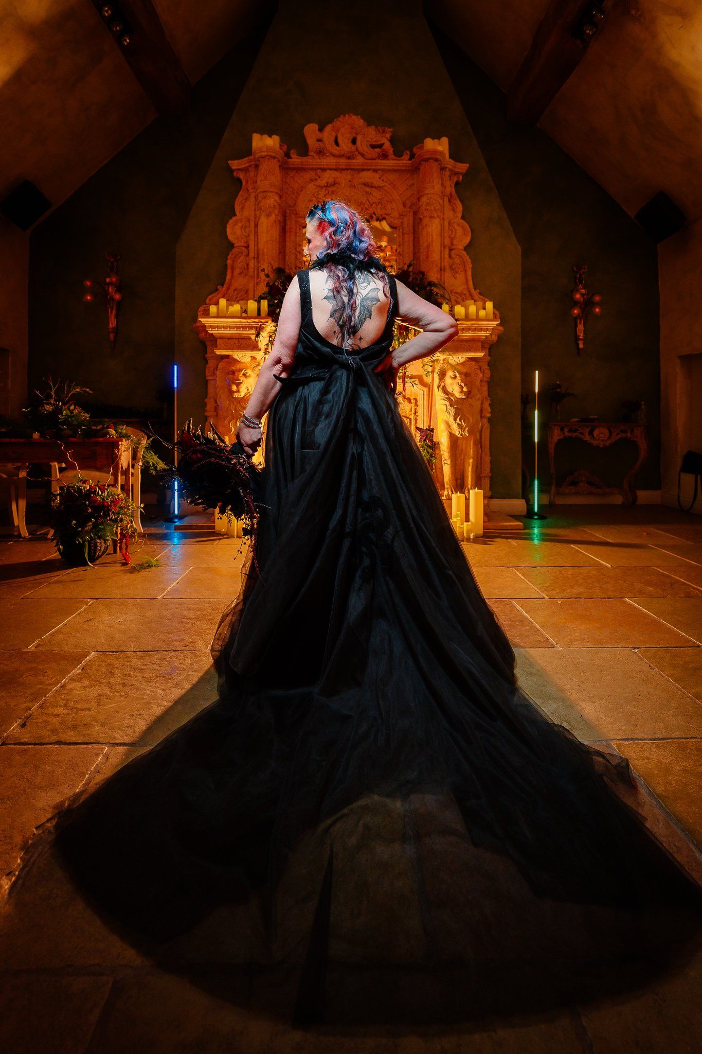 Bride in a black wedding dress with a long train standing before the candlelit fireplace at Le Petit Chateau