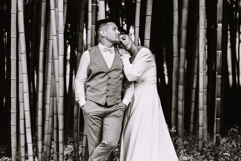 Portrait noir et blanc de la mariée appuyée contre le marié en gilet et nœud papillon, au milieu des herbes hautes