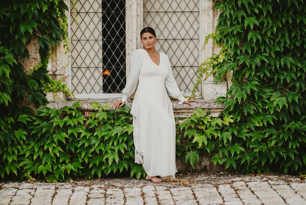 Mariée pieds nus en robe blanche à manches longues sur un chemin pavé