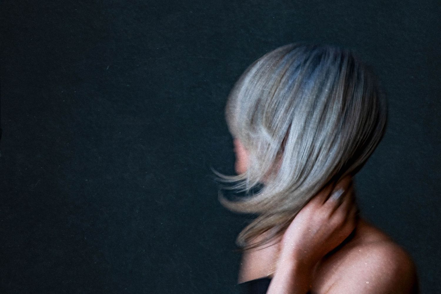 Woman with silver-gray bob haircut posing against dark background, hair sweeping across face.