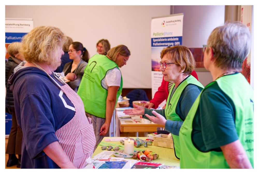 Freiwillige in grünen Westen unterstützen Besucher an einem Informationsstand während einer Gemeindeveranstaltung.