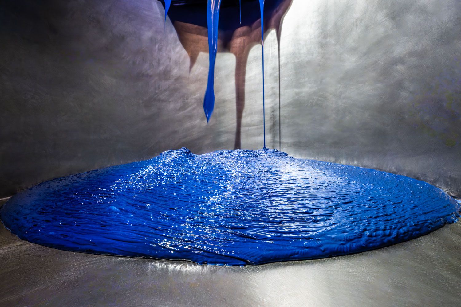 Blue liquid paint pouring and spreading on a metallic surface, creating a vibrant circular pool in paint factory