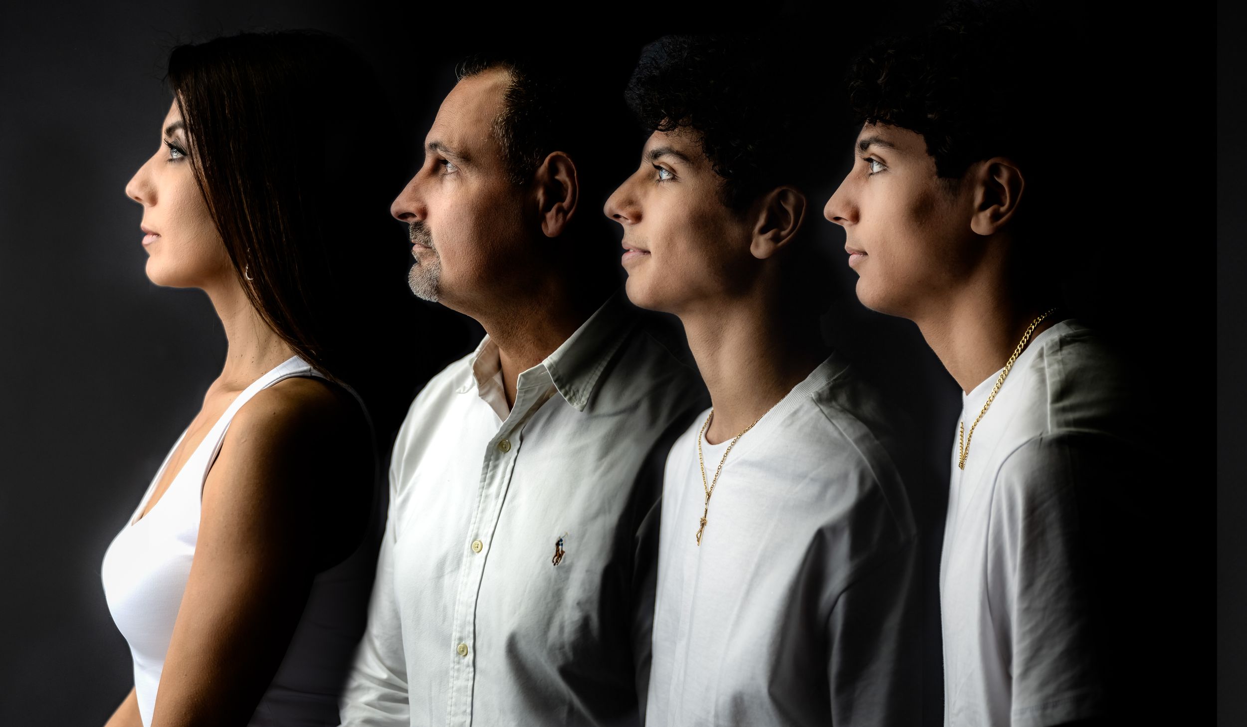 Four family members pose in profile against a dark background, captured in a dramatic side-view portrait.