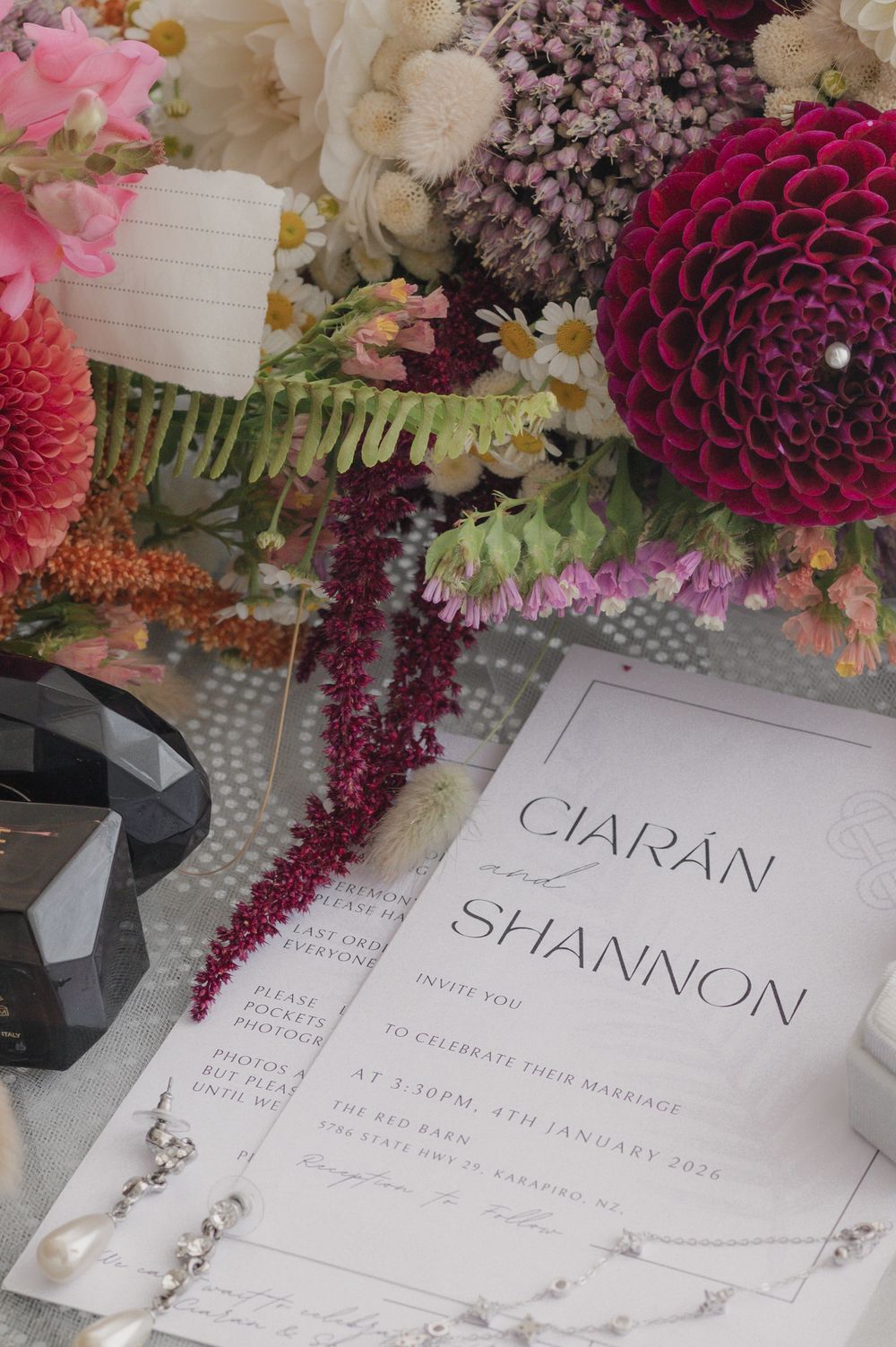 Wedding invitation for Ciaran and Shannon surrounded by colorful dahlias, jewelry, and floral arrangements.