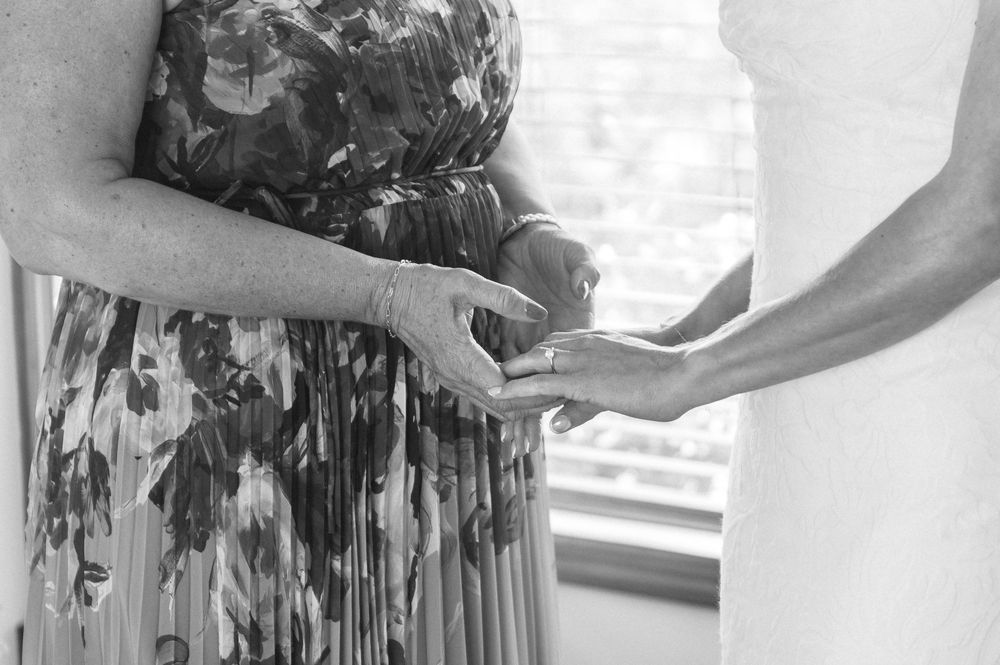 Black and white photo of two women holding hands in elegant dresses at a wedding ceremony.