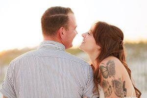 Couple sharing a romantic moment on a beach at sunset, woman with tattoos smiling at man in striped shirt.