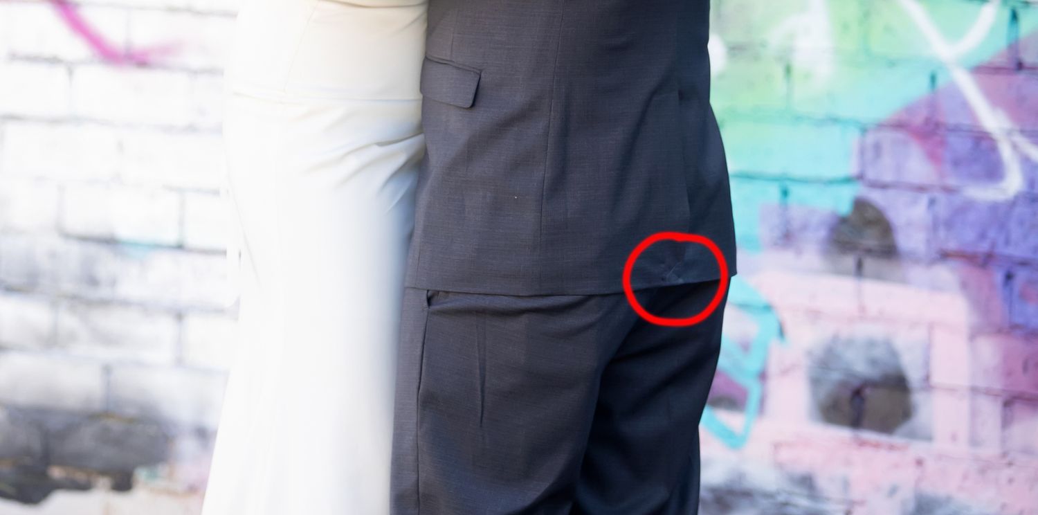Close-up of a man in a dark suit with a red circle highlighting a detail near the pocket, graffiti wall in background.