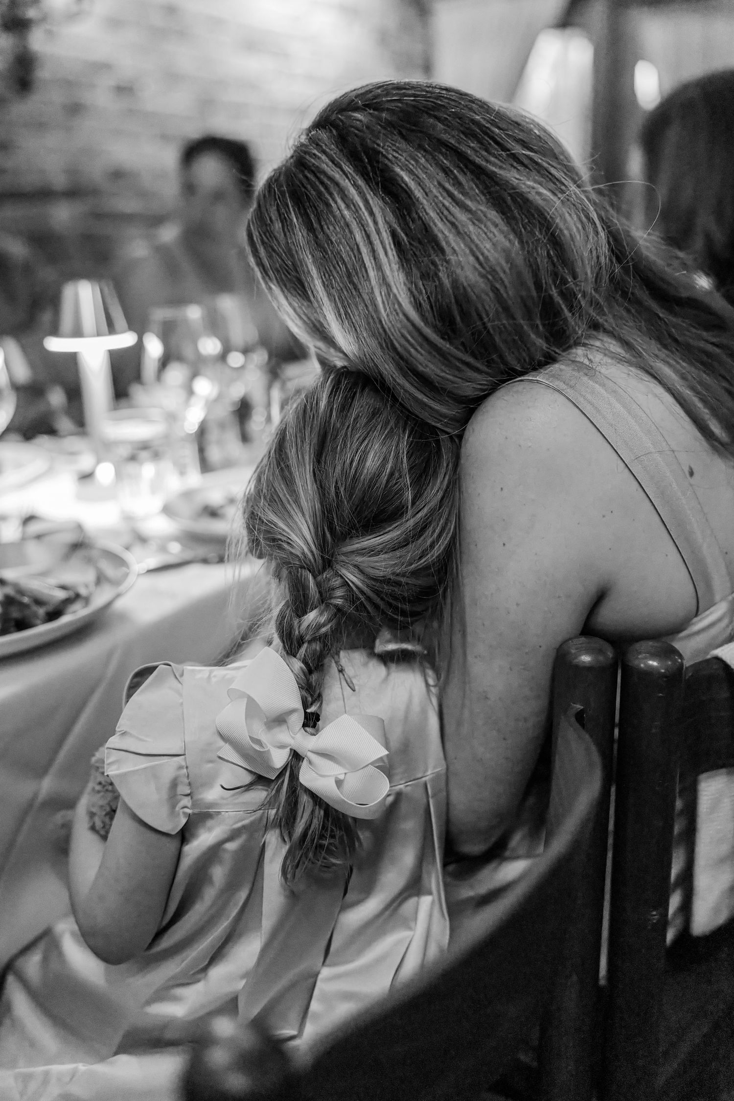 Black and white photo of a woman and young girl sharing a tender moment at a formal dinner event.