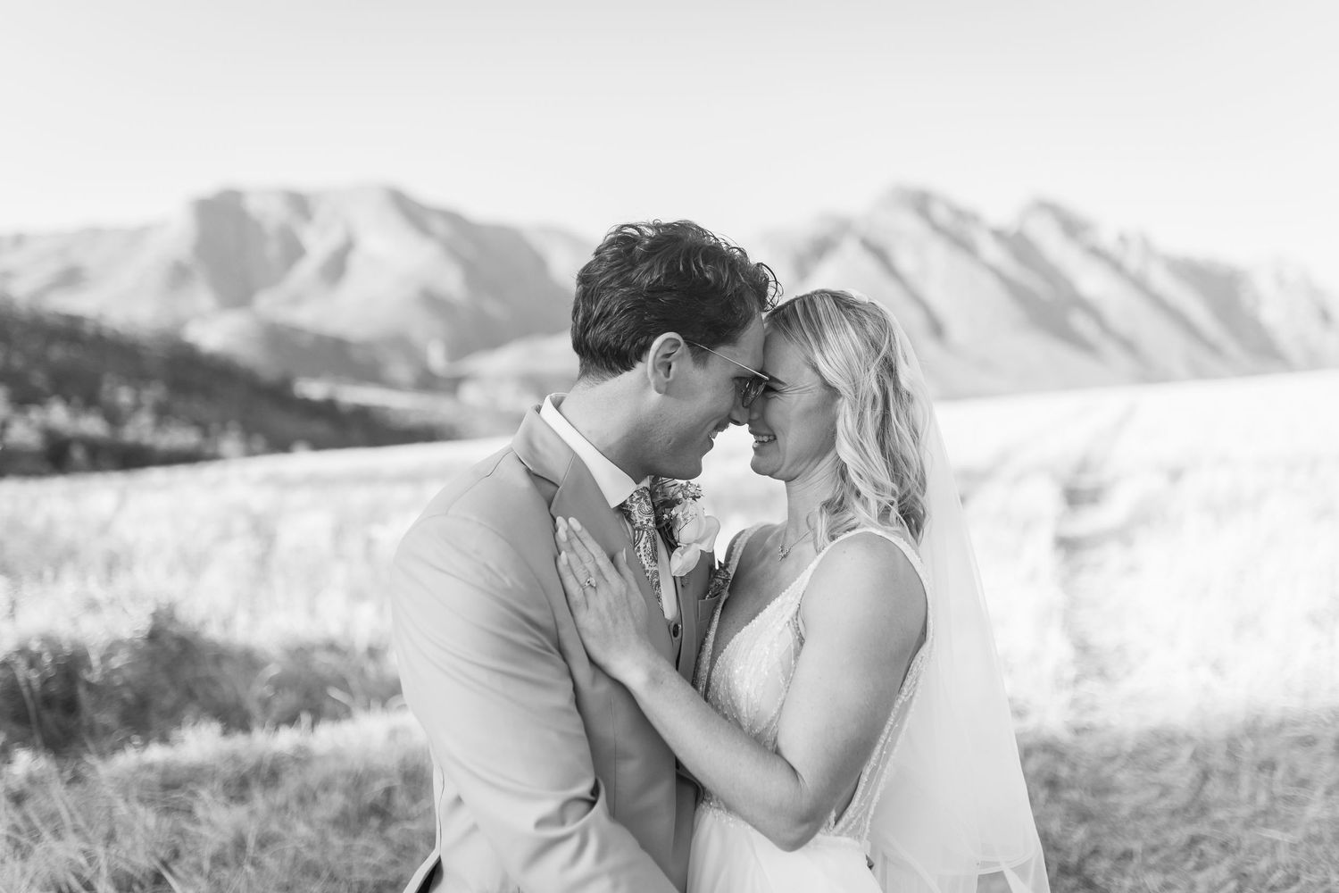 Black and white photo of a couple sharing a romantic moment with mountain peaks in the background at their outdoor wedding.