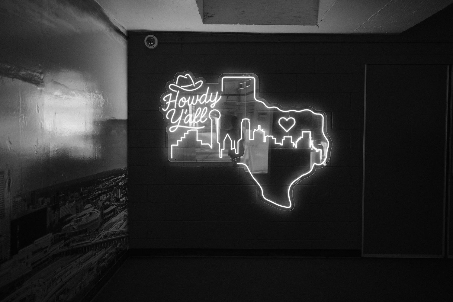 Neon sign of Texas state outline with cityscape and Howdy Yall text on dark wall.