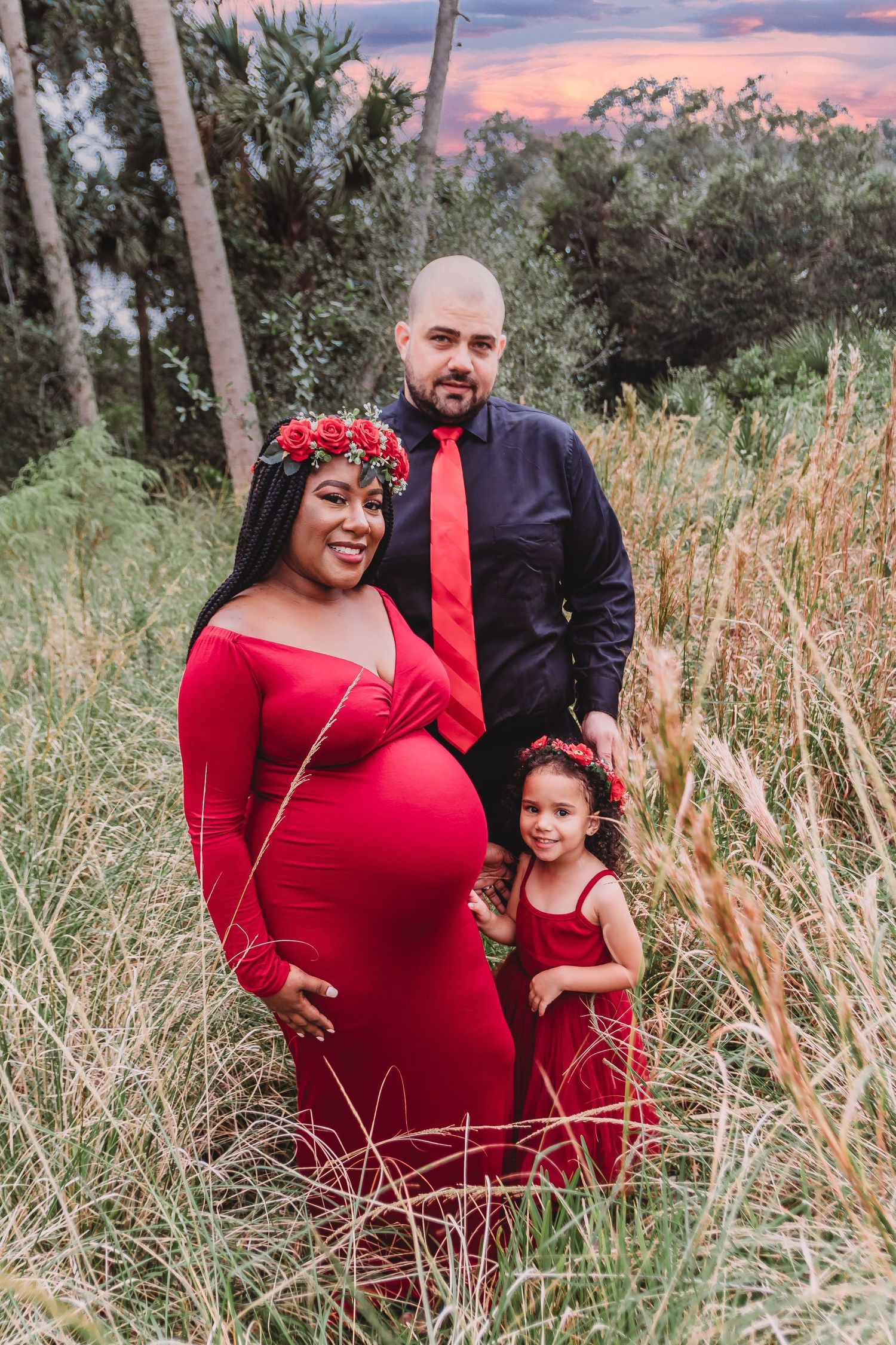 Maternity session in Jupiter riverbend park of a family in red smiling standing close in a field with daughter by Photogenic Fox Photography