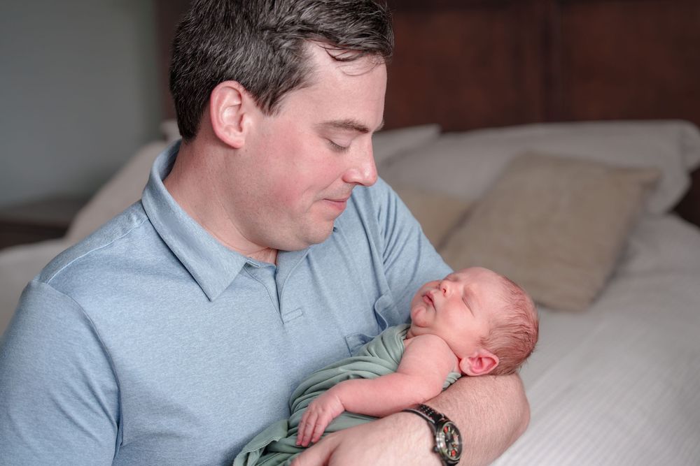 Dad newborn baby by the window natural light mom love cuddles candid posed black and white baby boy Dallas Texas big brother inhome session