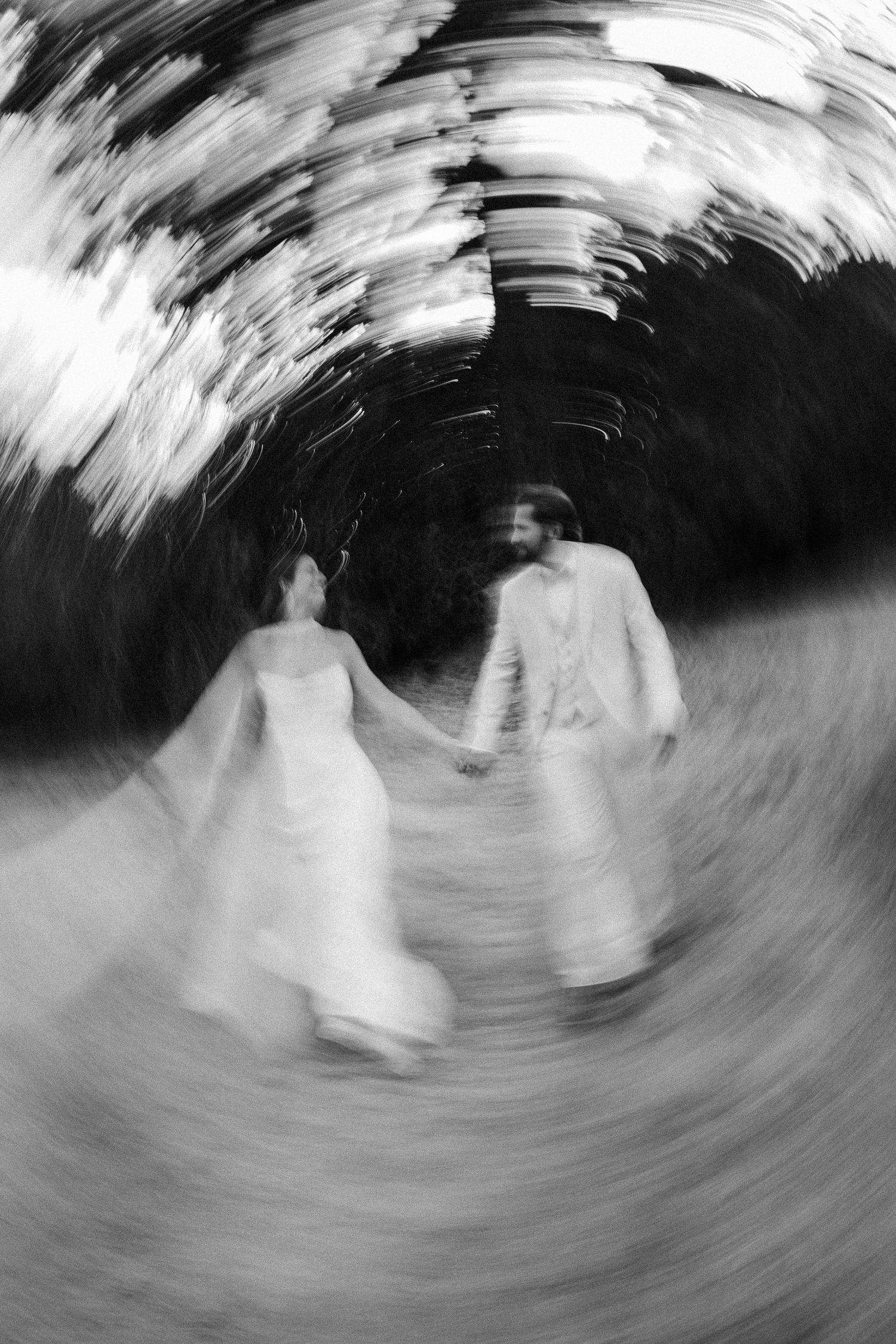 Black and white wedding photo with spin blur effect of bride and groom holding hands outdoors.