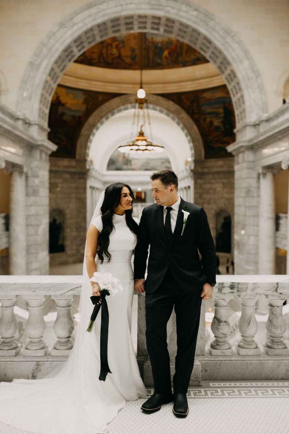 Bride and groom share a romantic moment on marble balcony inside an ornate capitol building rotunda.