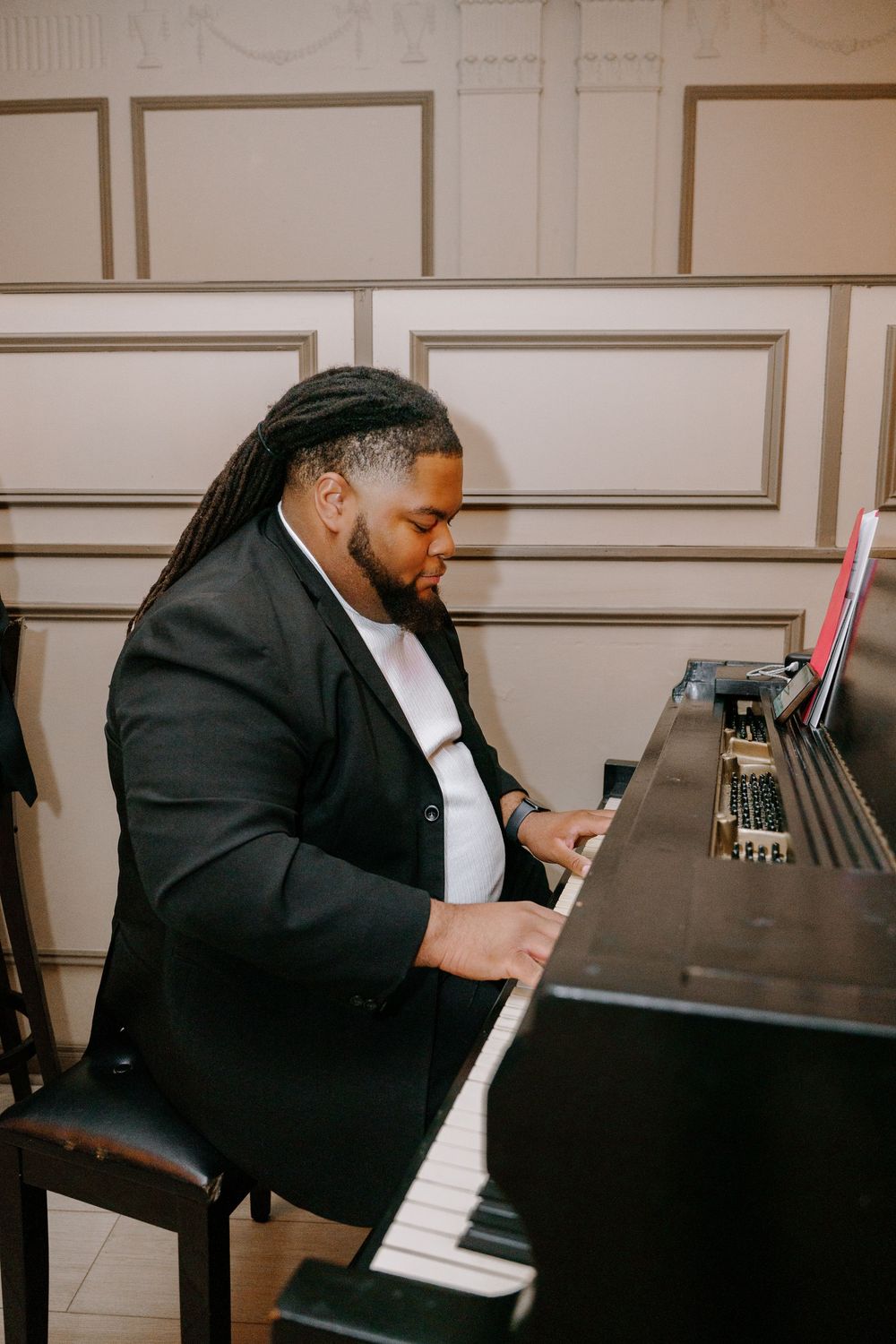 A musician with dreadlocks plays piano in a formal venue wearing a black blazer.
