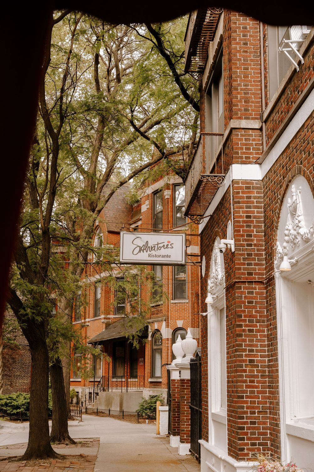 Salvatori's Restaurant sign on a charming red brick building along a tree-lined sidewalk in a historic neighborhood.