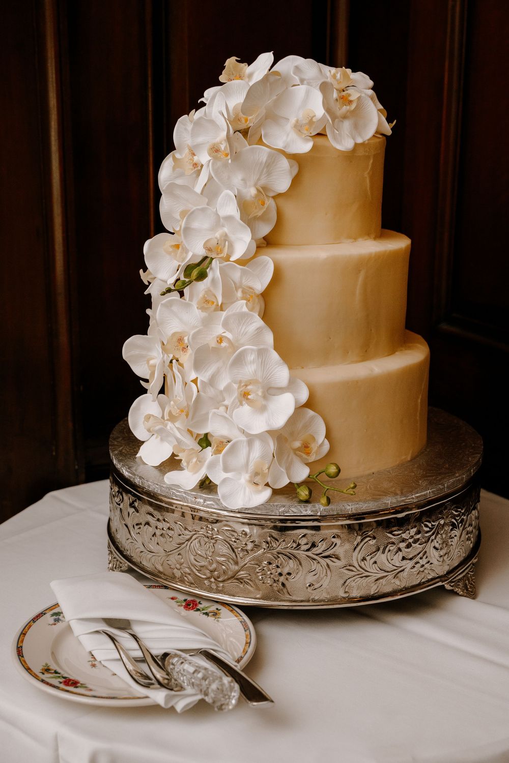Elegant three-tier gold wedding cake adorned with cascading white orchids on a silver stand.