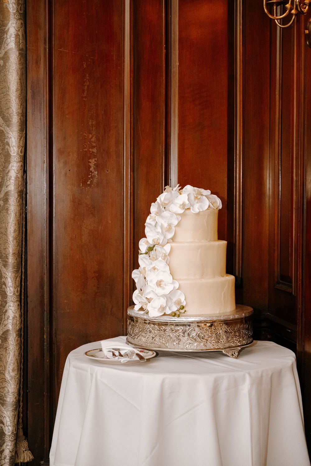 Elegant four-tier white wedding cake adorned with cascading white orchids on a silver stand.