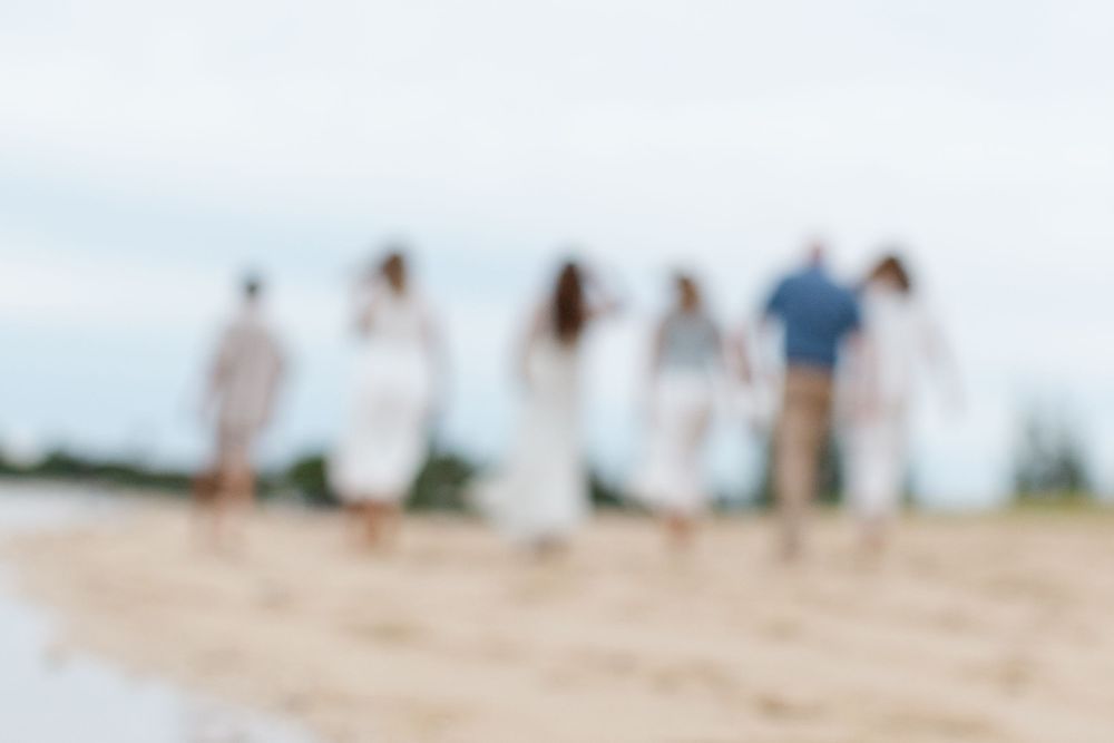 Blurred group of people walking on a sandy beach, dressed in white and casual attire on a cloudy day.
