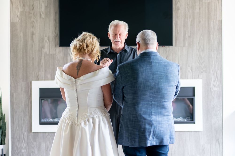 Officiant joining hands of bride and groom during intimate wedding ceremony by fireplace.