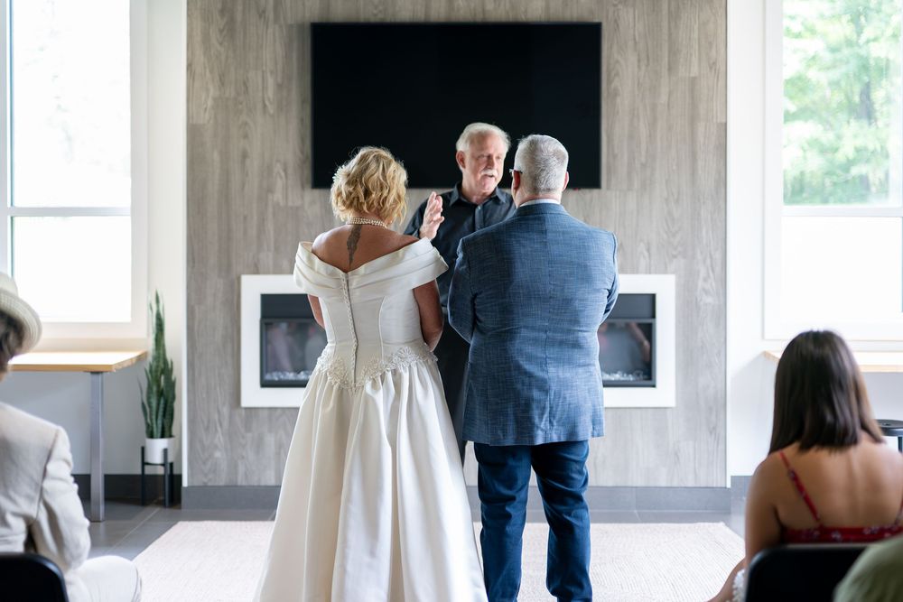 Officiant speaks with bride in white gown and groom in blue suit during intimate wedding ceremony.