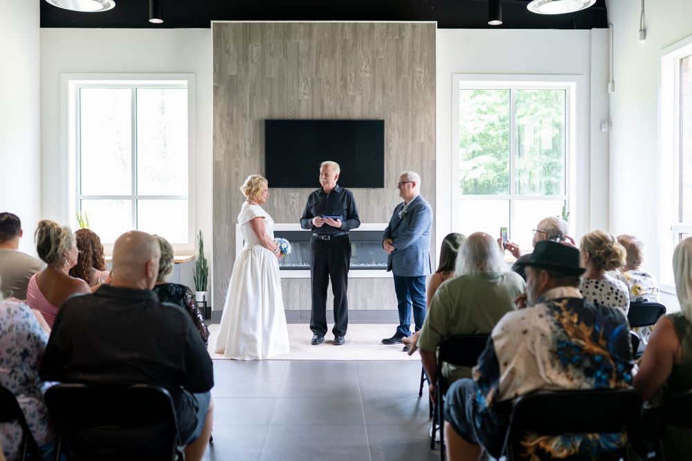 Elegant indoor wedding ceremony with bride in white gown and groom before officiant, guests seated in modern venue.