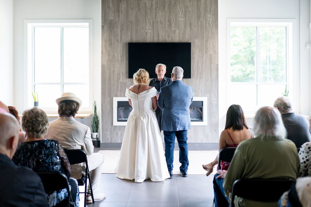 Bride in white gown and groom stand before guests during intimate indoor wedding ceremony.