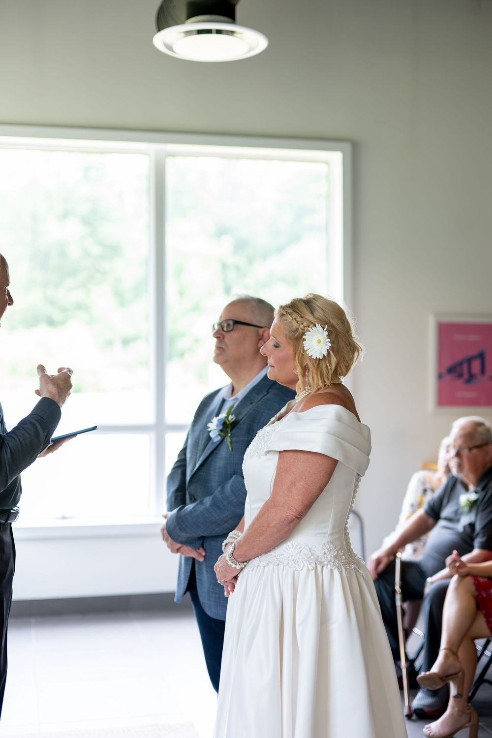 Bride and groom stand at altar during intimate wedding ceremony with seated guests nearby.