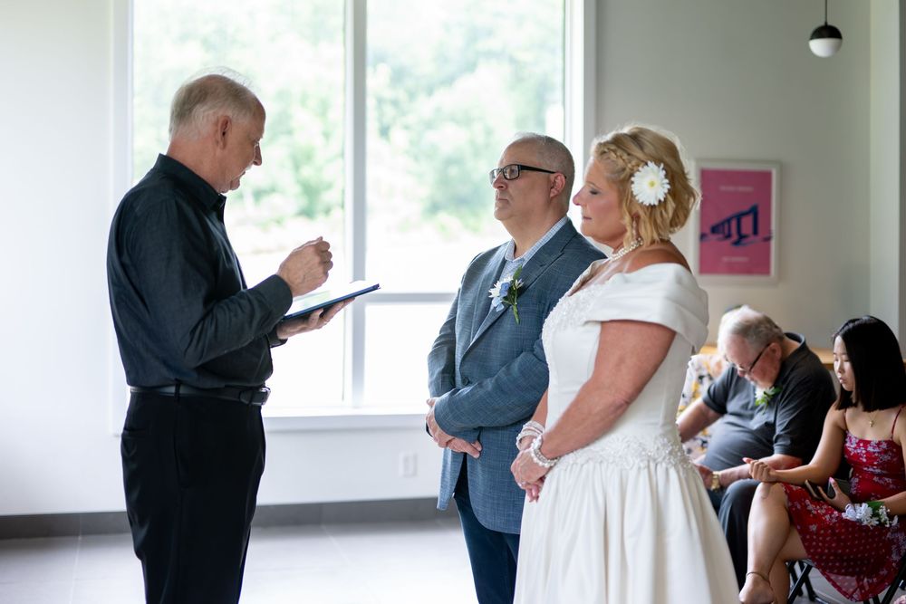 An officiant reads from a book during a small wedding ceremony as the couple stands attentively.