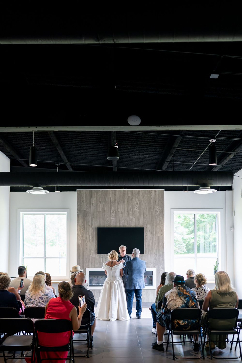 Wide shot of small wedding ceremony with bride and groom at altar before seated guests.