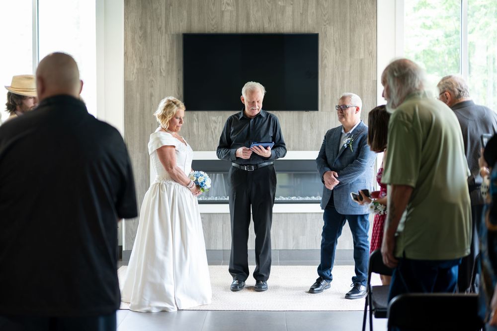 Wedding officiant reads vows as bride and groom stand before small gathered guests indoors.