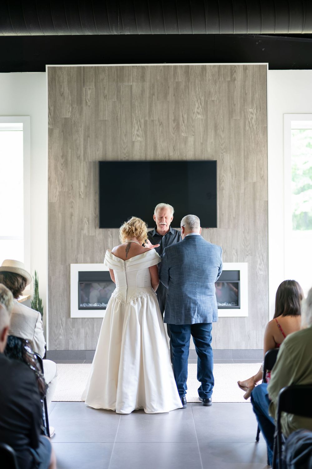 A bride and groom stand before an officiant during an intimate wedding ceremony indoors.
