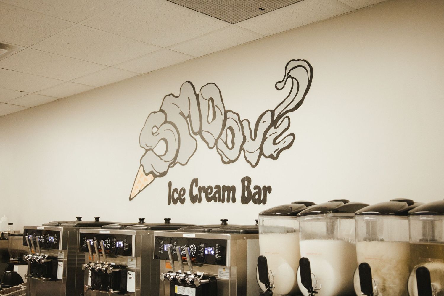 Snoove Ice Cream Bar wall logo above a row of soft-serve machines in a bright, modern ice cream shop.
