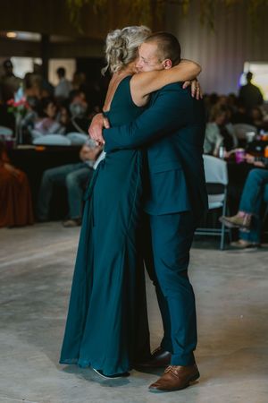 A couple shares an emotional dance at a wedding reception, both dressed in teal outfits, embracing warmly on the dance floor.