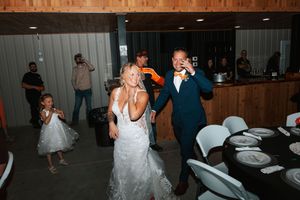 Bride in white gown and groom in navy suit share a joyful first dance at their rustic wedding reception.