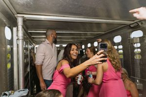Bridesmaids in pink dresses taking a selfie with a man inside a horse trailer at a wedding.