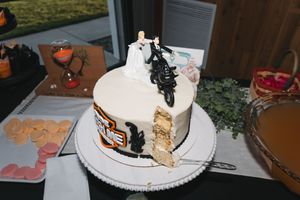 Wedding groom cake decorated with Harley-Davidson motorcycle design and bride and groom cake topper, partially sliced.