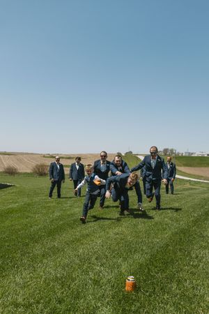 Groomsmen in navy suits playing a lawn game outdoors on a sunny day at a countryside wedding venue.