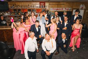 Wedding party celebrating at Cromwell Taps bar, bridesmaids in pink gowns and groomsmen in navy suits raising glasses.