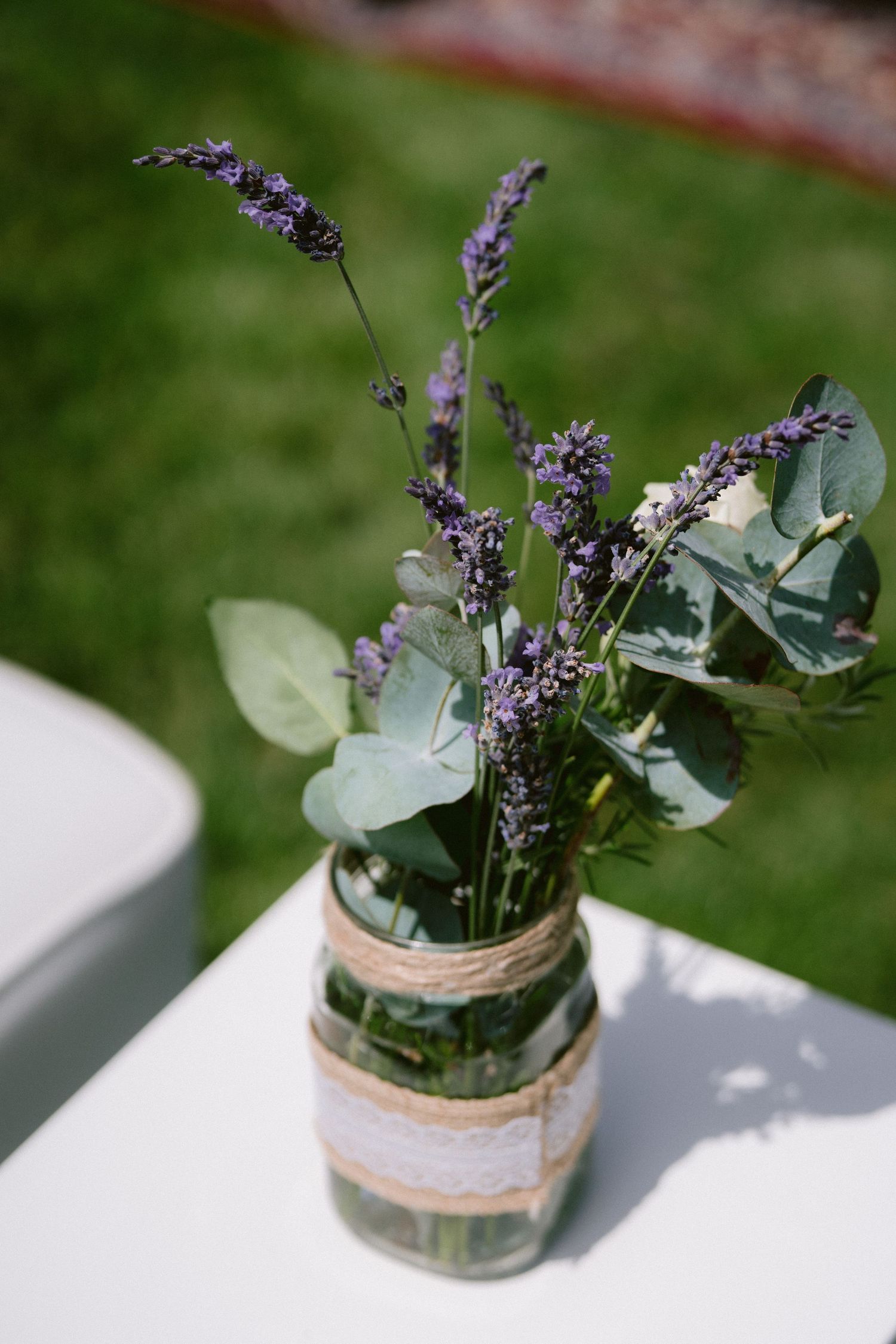 Mason jar with lavender and eucalyptus wrapped in twine and lace on white table.